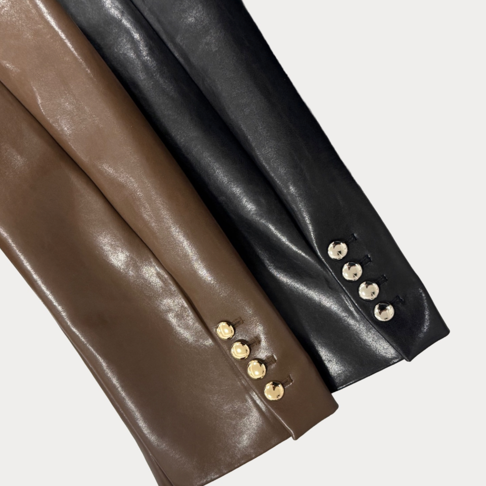 Close-up of two faux leather blazer sleeves, one in brown and one in black, both detailed with gold-tone metal snap buttons near the cuffs, set against a light gray background.