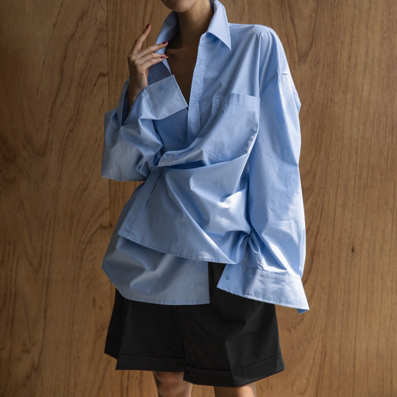 Person wearing a blue oversized shirt over a black skirt against a wooden background
