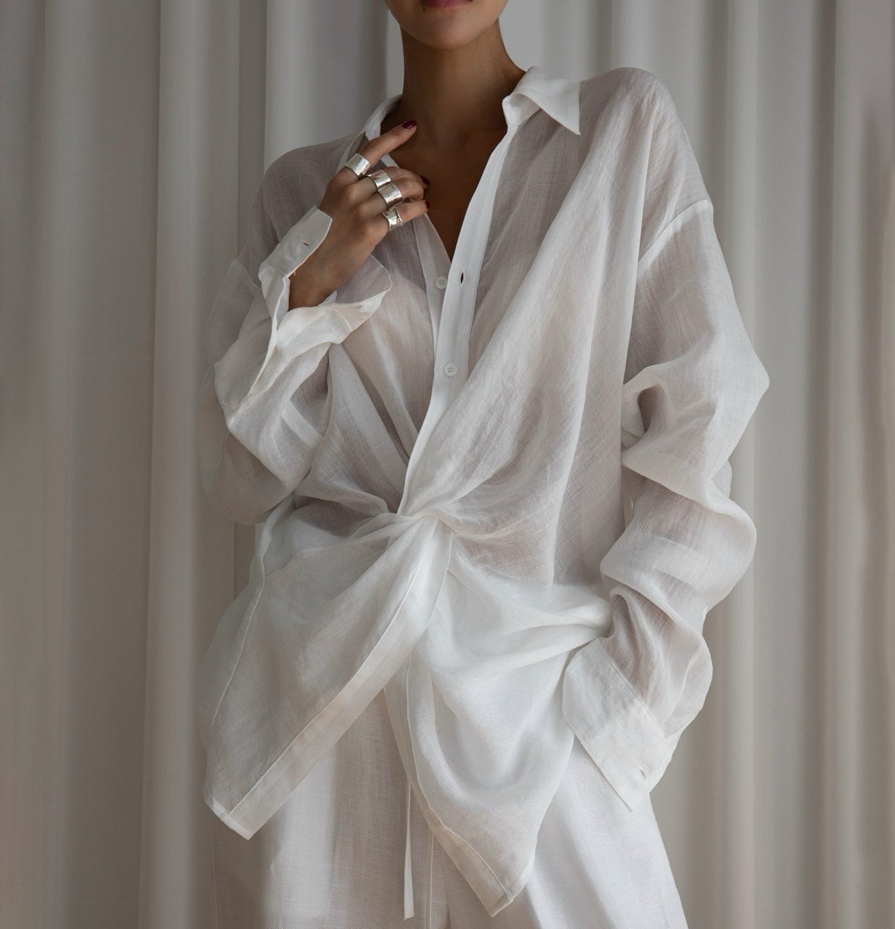 White sheer shirt with a knot detail worn by a person against a neutral background