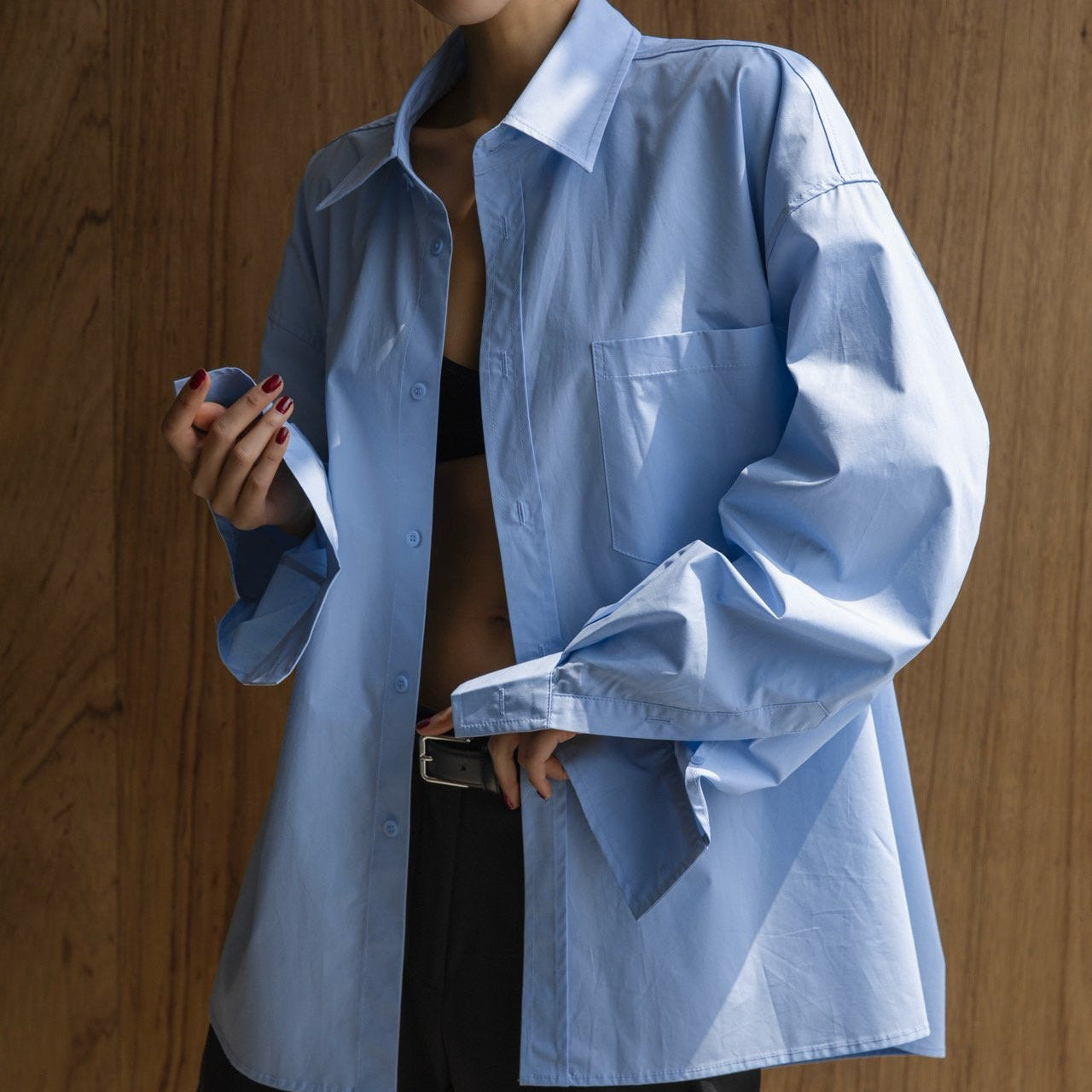 Person wearing a light blue oversized shirt against a wooden background