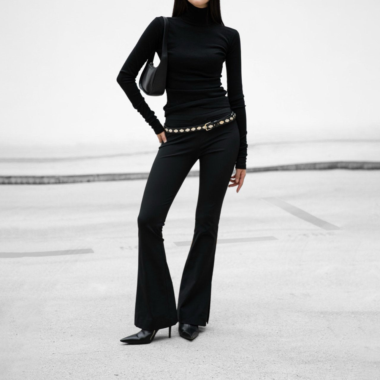 Person wearing a black outfit with flared pants on a light gray background