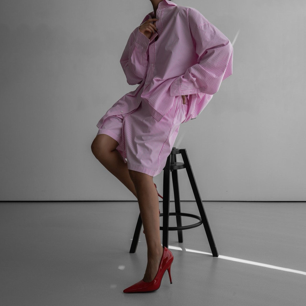Person wearing a pink dress with a black stool against a gray background