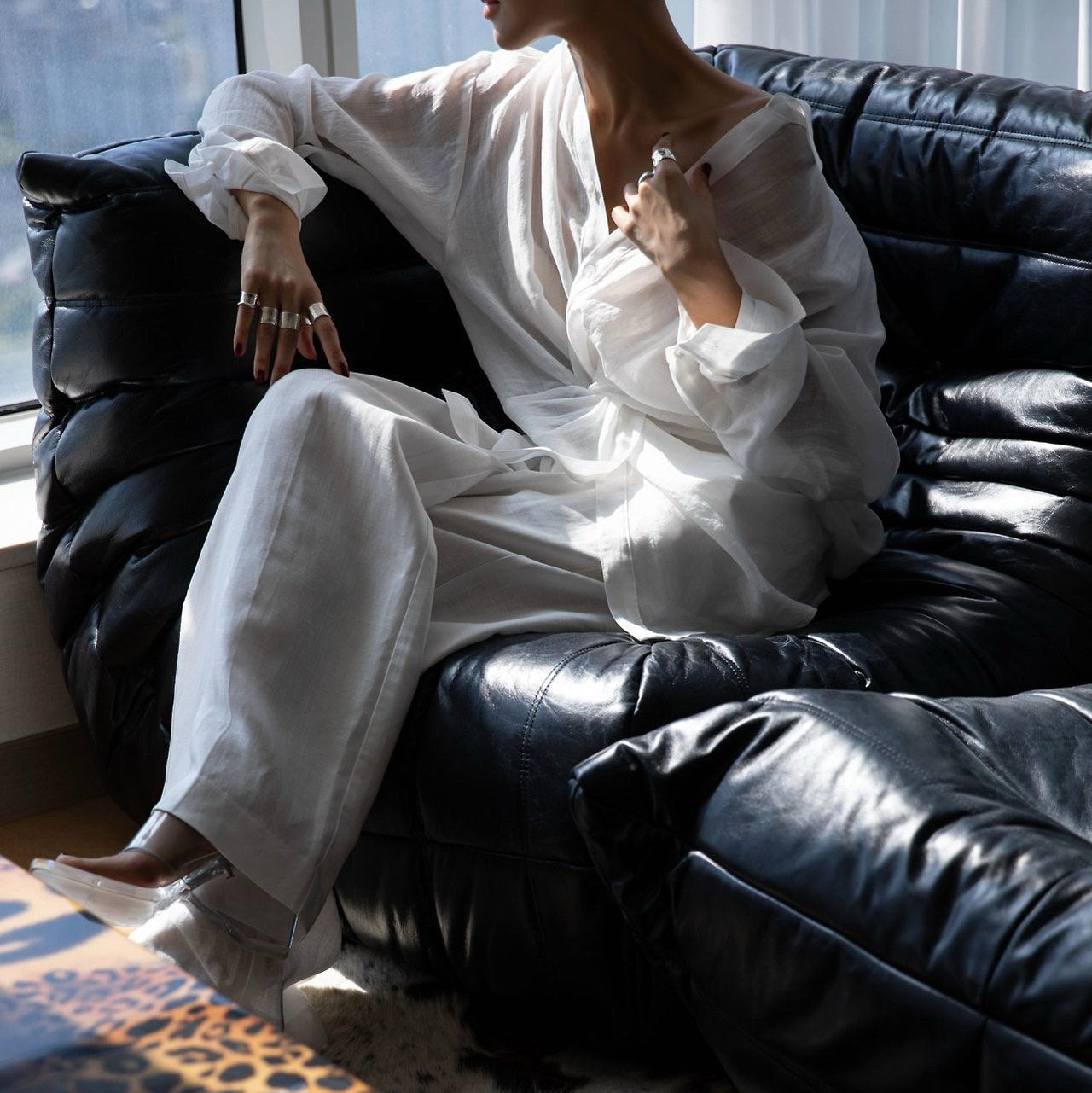 Person in a white outfit sitting on a black leather couch with a leopard print rug.