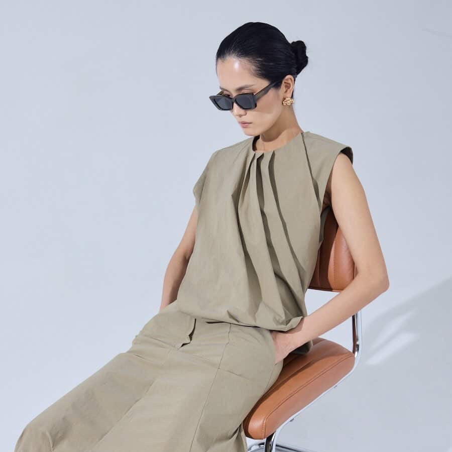 Woman in beige outfit sitting on a chair against a white background