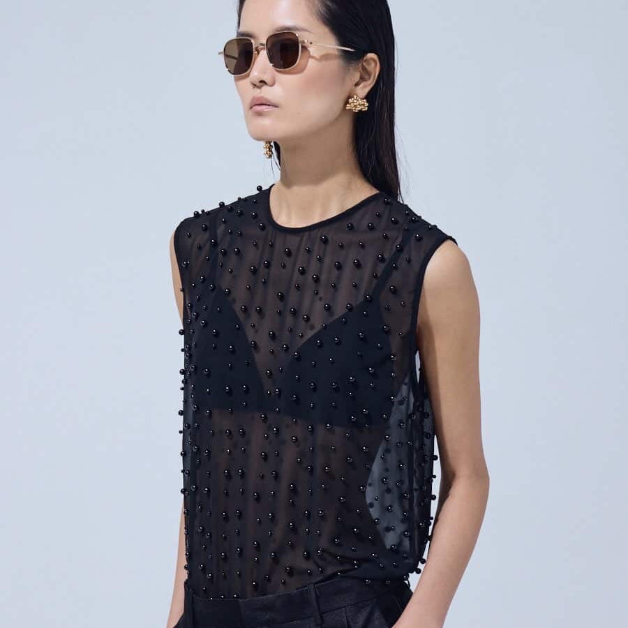 Woman wearing a black sleeveless top with bead details against a light gray background