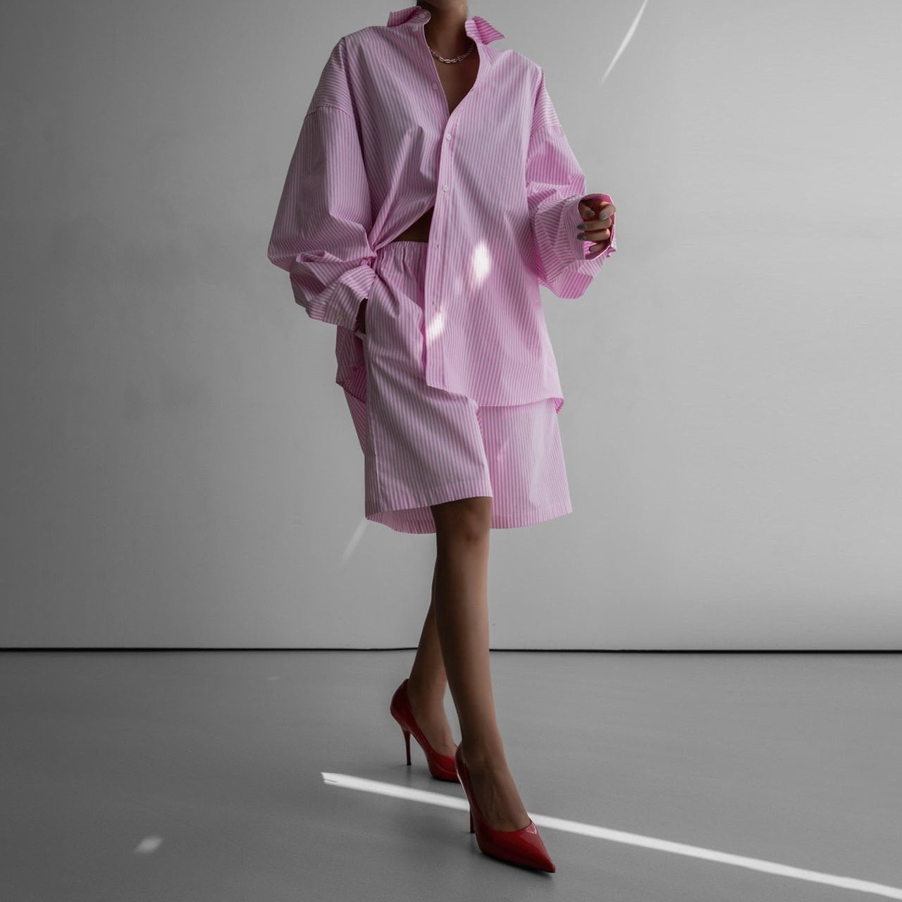 Person wearing a pink outfit with red high heels on a gray background