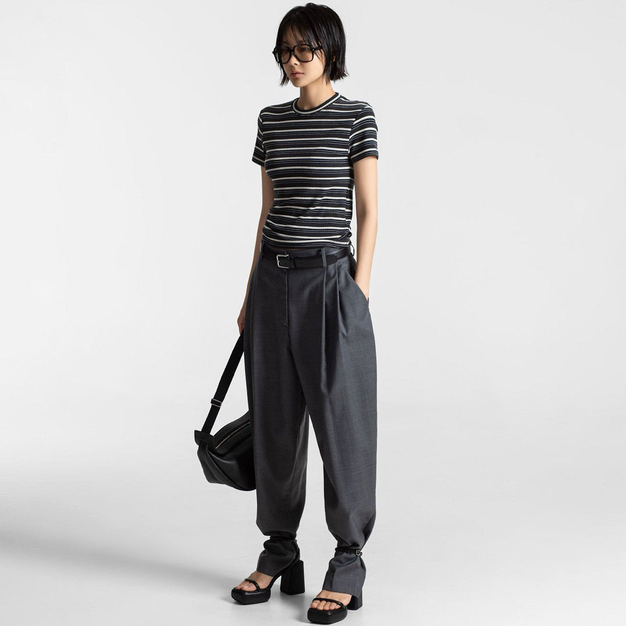 Person wearing a striped shirt and gray pants holding a black bag on a white background