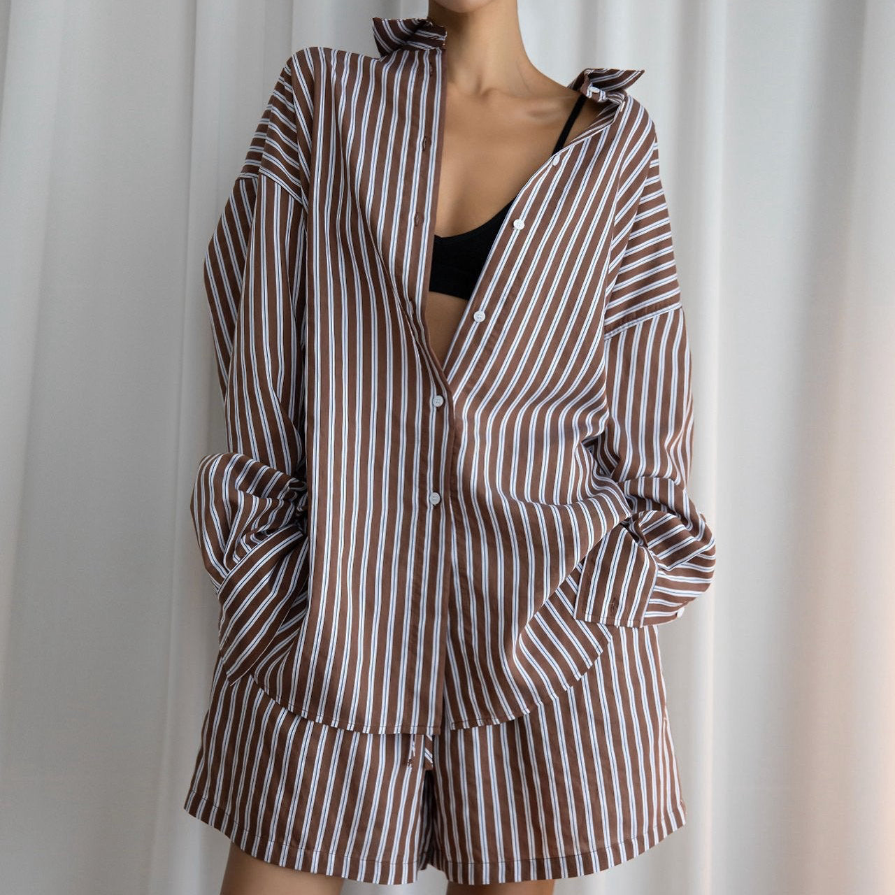 Person wearing a brown and white striped outfit against a white curtain background