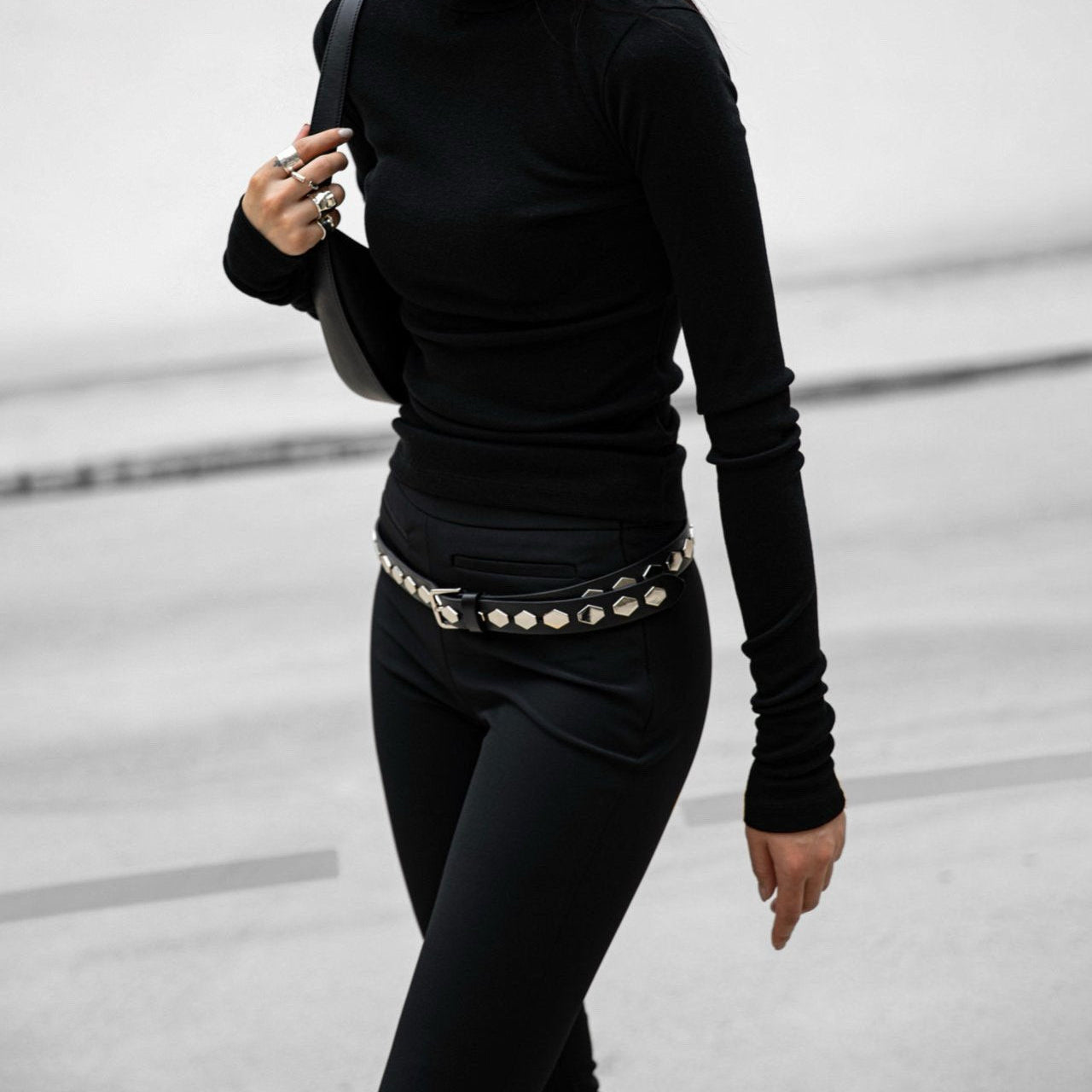 Person wearing a black turtleneck and pants with a belt, standing against a light background