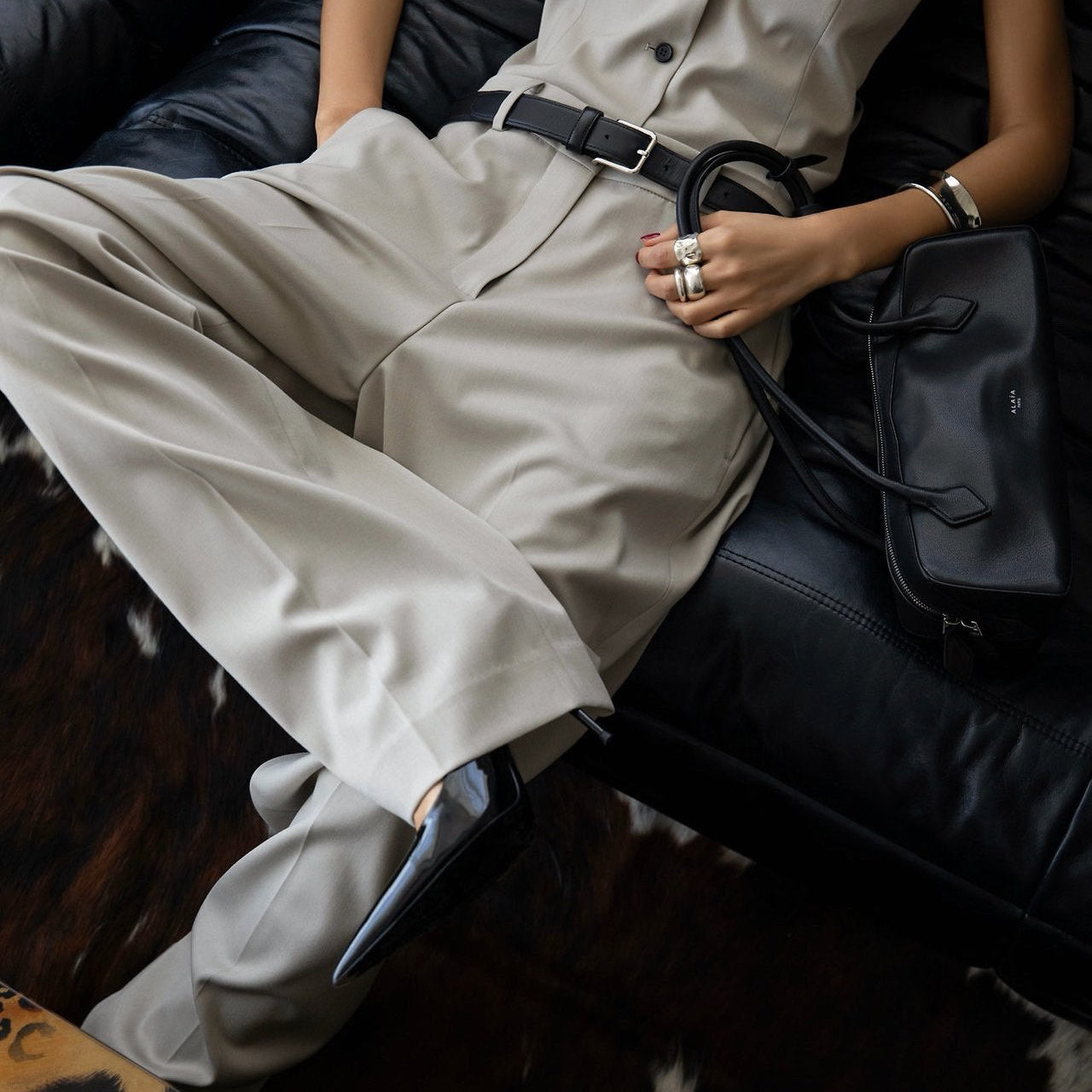 Person wearing a beige outfit with a black handbag on a dark surface
