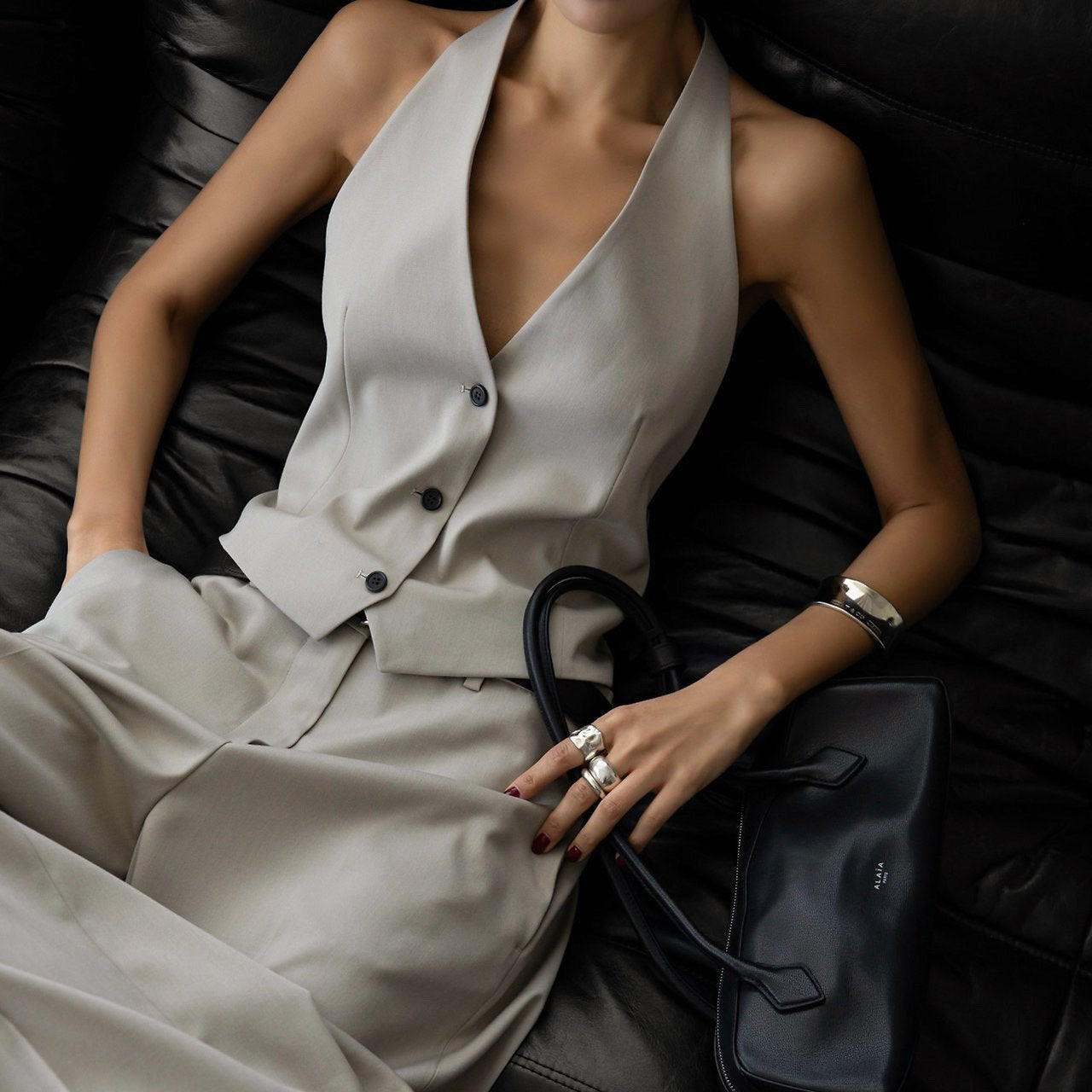 Person wearing a beige jumpsuit sitting on a black leather couch.
