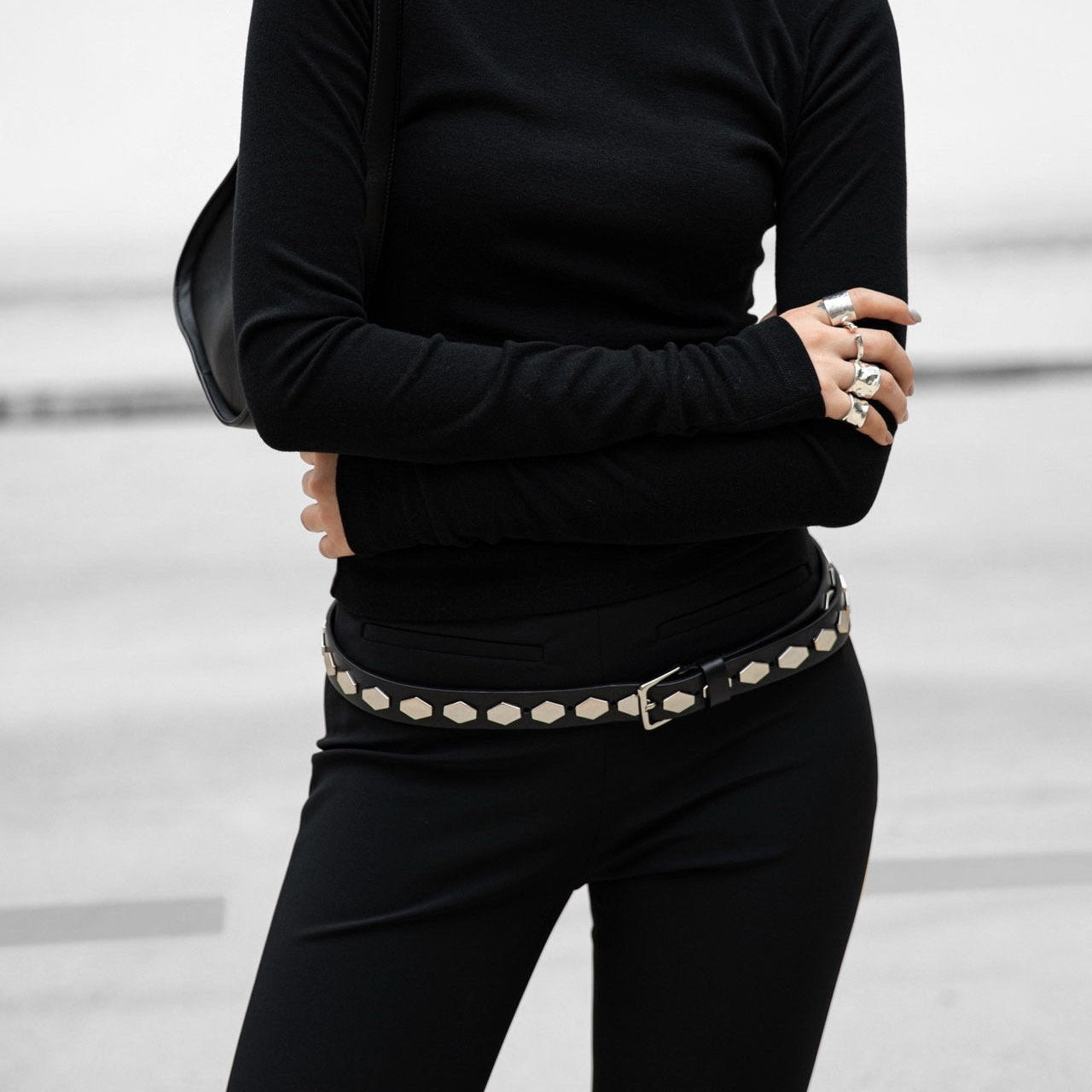 Person wearing a black turtleneck and black pants with a decorative belt against a light background